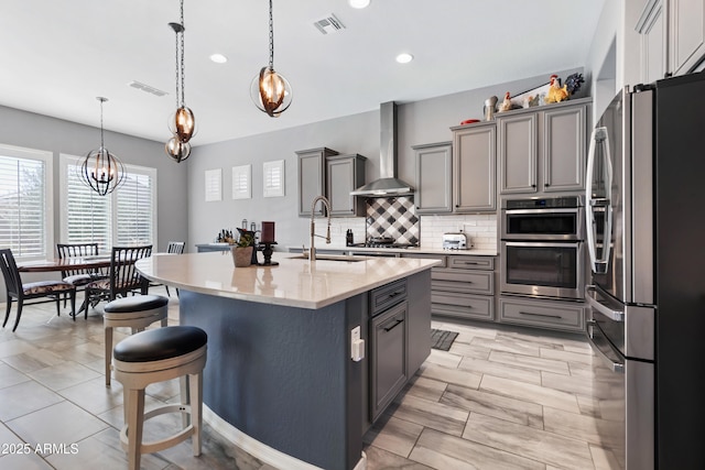 kitchen with appliances with stainless steel finishes, a breakfast bar, gray cabinets, wall chimney range hood, and a sink