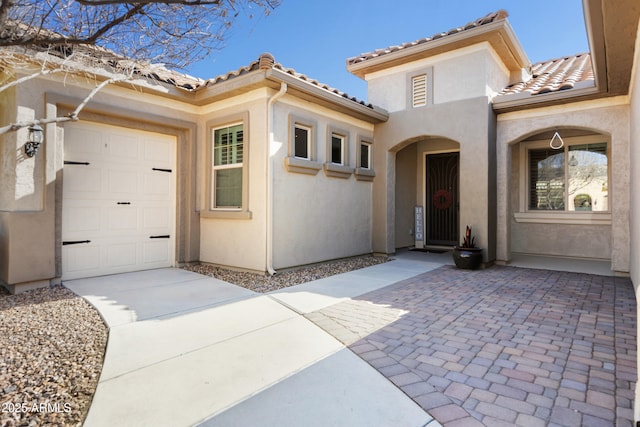 entrance to property with a garage, stucco siding, concrete driveway, and a tiled roof