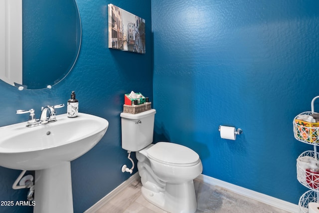 bathroom featuring baseboards, a textured wall, a sink, and toilet