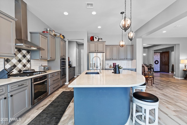 kitchen featuring stainless steel appliances, gray cabinets, visible vents, wall chimney range hood, and a kitchen bar