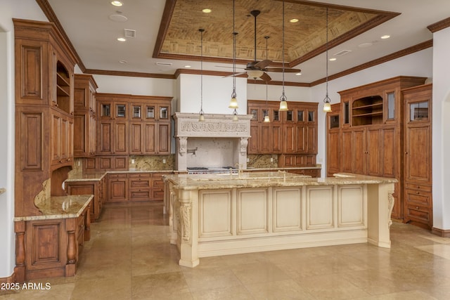 kitchen featuring pendant lighting, a raised ceiling, a large island with sink, and crown molding