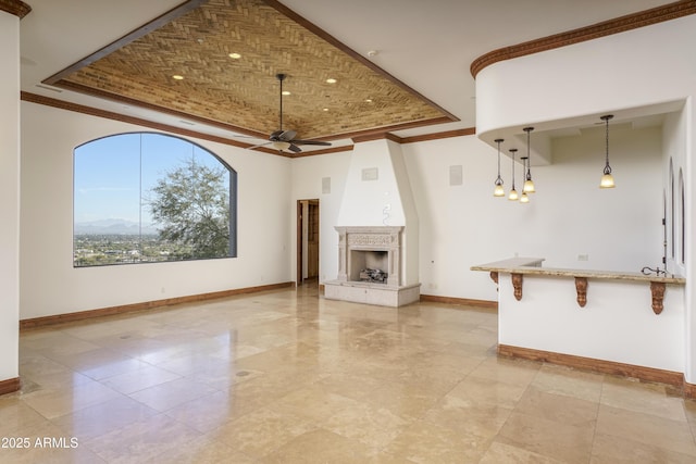 unfurnished living room with a raised ceiling, ceiling fan, and ornamental molding