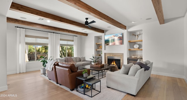 living room with beamed ceiling, light hardwood / wood-style flooring, a tiled fireplace, and ceiling fan