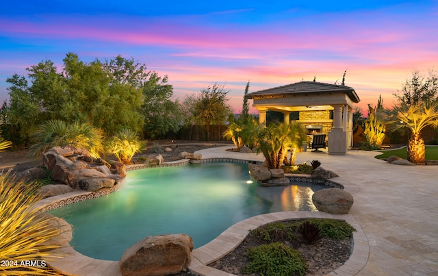 pool at dusk with a gazebo and a patio area