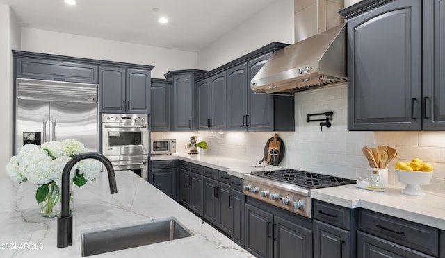 kitchen with stainless steel appliances, backsplash, sink, ventilation hood, and light stone counters