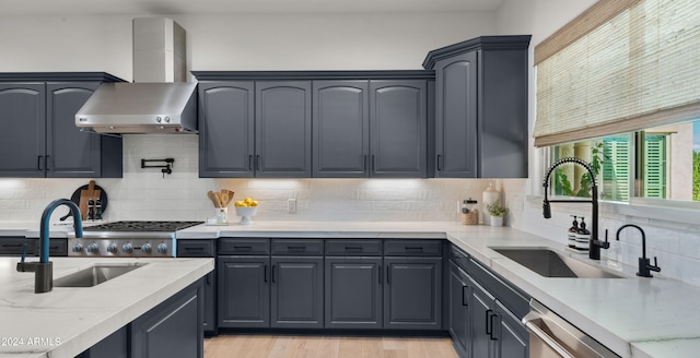 kitchen featuring wall chimney range hood, sink, appliances with stainless steel finishes, backsplash, and light hardwood / wood-style floors