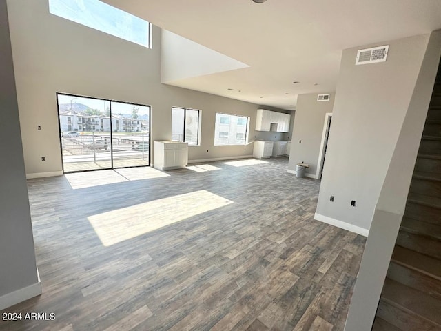 unfurnished living room with dark hardwood / wood-style floors, a towering ceiling, and plenty of natural light