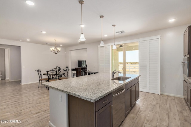 kitchen with light stone counters, sink, stainless steel dishwasher, and an island with sink