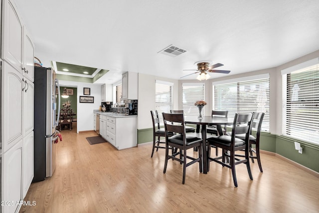 dining room with light wood-type flooring, a tray ceiling, a healthy amount of sunlight, and visible vents