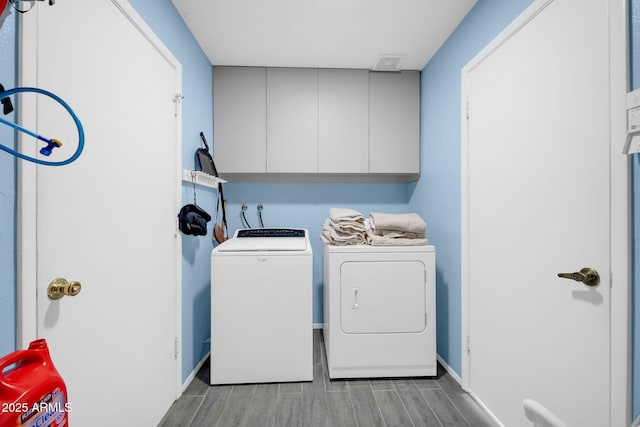 washroom featuring wood finish floors, washing machine and clothes dryer, cabinet space, and baseboards