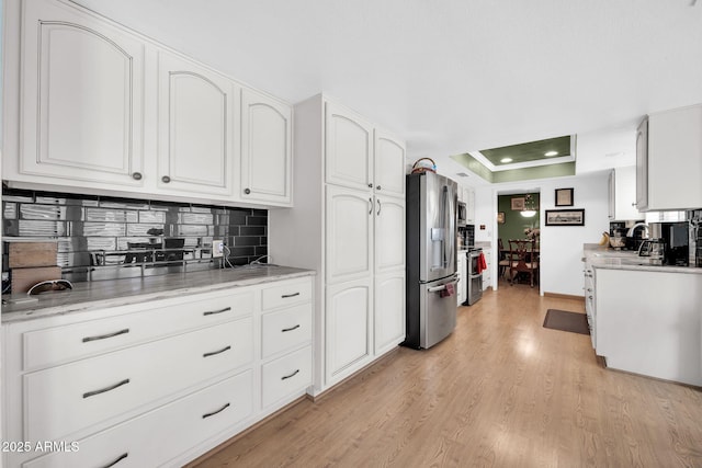 kitchen featuring light wood finished floors, a raised ceiling, appliances with stainless steel finishes, white cabinetry, and backsplash