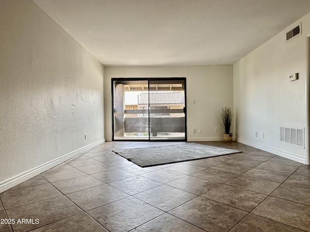 tiled empty room featuring baseboards, visible vents, and a textured wall