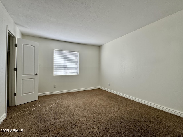 spare room featuring a textured ceiling, dark colored carpet, and baseboards