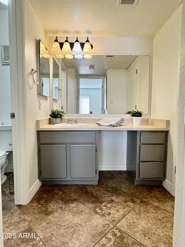 bathroom with visible vents, toilet, vanity, a textured ceiling, and baseboards