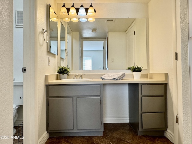 bathroom featuring baseboards, visible vents, a textured wall, toilet, and vanity