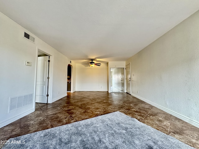 empty room featuring ceiling fan, visible vents, arched walkways, and baseboards