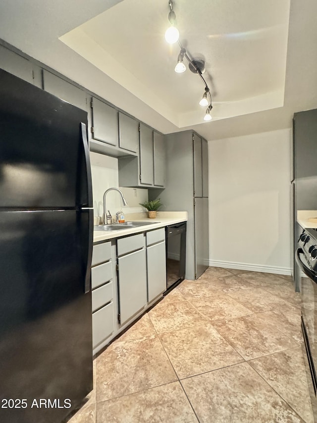 kitchen featuring a raised ceiling, light countertops, gray cabinetry, a sink, and black appliances