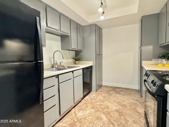 kitchen featuring a tray ceiling, gray cabinets, light countertops, a sink, and black appliances