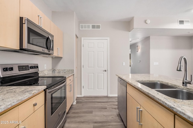 kitchen with sink, stainless steel appliances, light stone counters, light hardwood / wood-style floors, and light brown cabinets