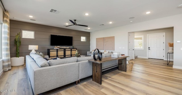 living room featuring ceiling fan, wood walls, and light hardwood / wood-style floors