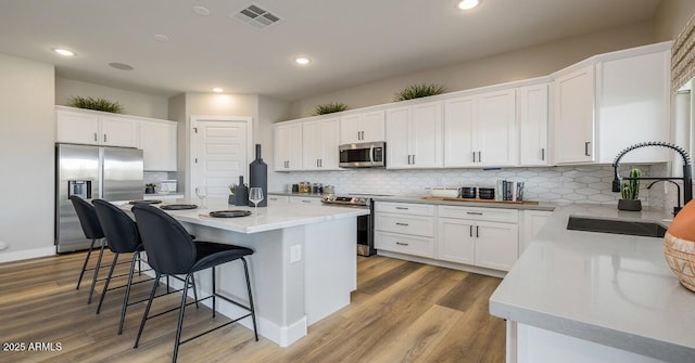 kitchen featuring stainless steel appliances, white cabinets, a kitchen island, light hardwood / wood-style flooring, and sink