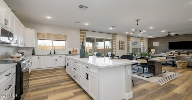 kitchen with appliances with stainless steel finishes, white cabinets, a kitchen island, light hardwood / wood-style flooring, and sink