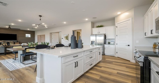 kitchen with white cabinetry, stainless steel appliances, hanging light fixtures, light stone countertops, and a kitchen island