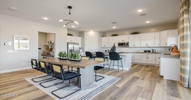 dining space with light wood-type flooring, an inviting chandelier, and sink