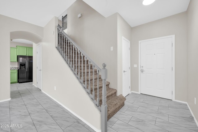 foyer featuring stairway, arched walkways, marble finish floor, and baseboards