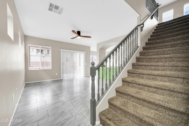 stairway featuring plenty of natural light, baseboards, visible vents, and ceiling fan