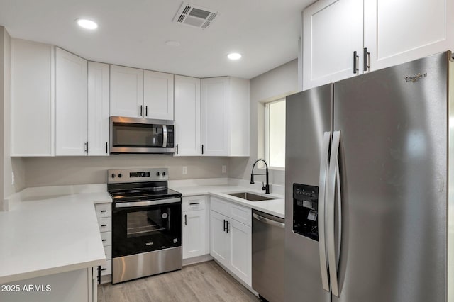 kitchen featuring white cabinetry, sink, light hardwood / wood-style flooring, and appliances with stainless steel finishes