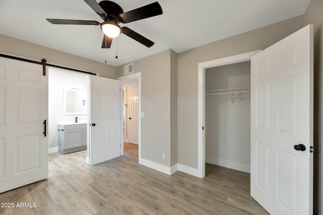 unfurnished bedroom featuring sink, light wood-type flooring, a closet, ceiling fan, and a barn door