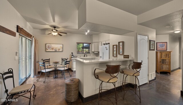 2311 W Dobbins Rd, Phoenix, AZ 85041 - kitchen featuring white refrigerator with ice dispenser, concrete floors, a peninsula, a breakfast bar area, and light countertops
