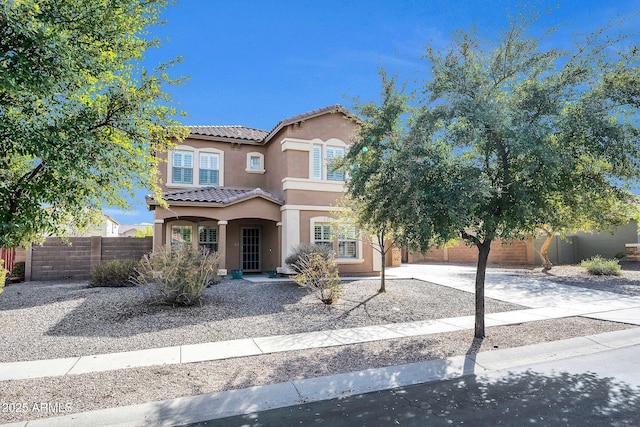 mediterranean / spanish home featuring a tiled roof, fence, concrete driveway, and stucco siding