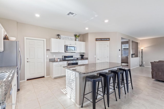 kitchen featuring a kitchen bar, white cabinetry, a kitchen island, stone counters, and stainless steel appliances