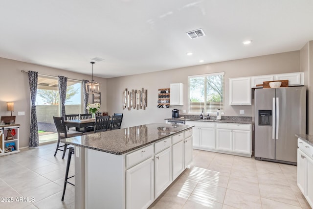 kitchen with pendant lighting, dark stone countertops, stainless steel refrigerator with ice dispenser, white cabinets, and a kitchen island