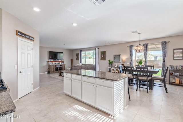 kitchen with white cabinetry, dark stone countertops, a kitchen breakfast bar, a kitchen island, and pendant lighting