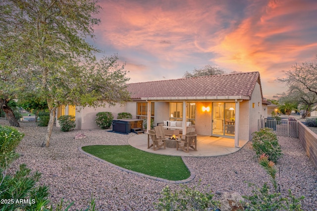 back of house at dusk featuring a hot tub, a fenced backyard, a tiled roof, a patio area, and stucco siding