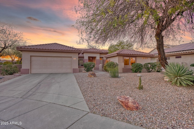 mediterranean / spanish-style house with a garage, driveway, a tiled roof, and stucco siding