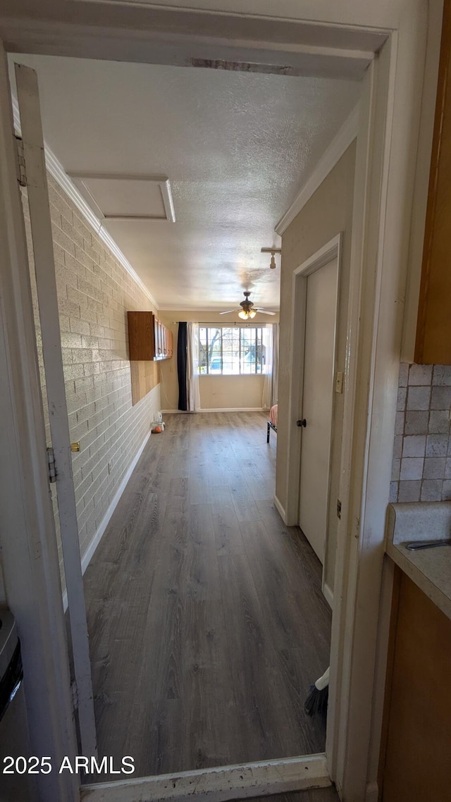 hallway featuring wood finished floors, a textured ceiling, ornamental molding, and brick wall