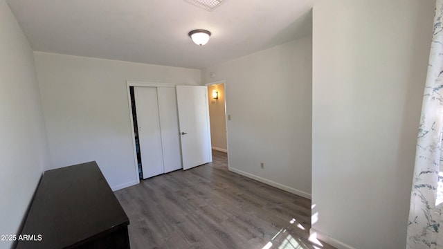 unfurnished bedroom featuring wood finished floors, visible vents, a closet, and baseboards