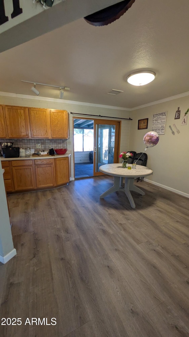 kitchen featuring dark wood-style floors, baseboards, brown cabinets, crown molding, and tasteful backsplash