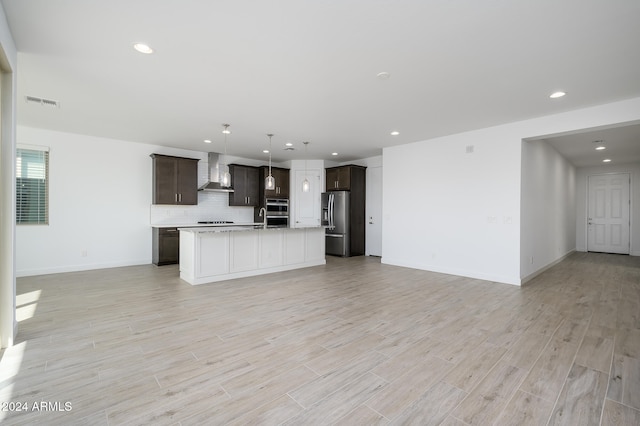 kitchen with wall chimney exhaust hood, light wood-type flooring, stainless steel fridge with ice dispenser, and a kitchen island with sink