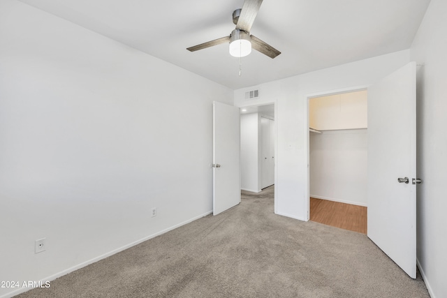 unfurnished bedroom featuring ceiling fan, a closet, light carpet, and a spacious closet