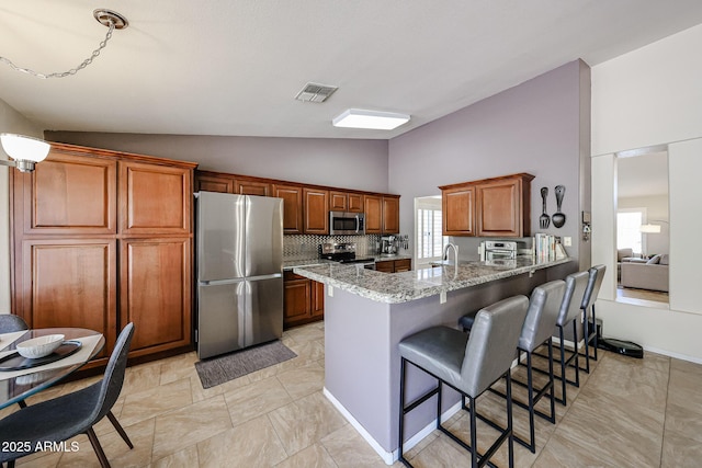 4558 E Libby St, Phoenix, AZ 85032 - kitchen featuring stainless steel appliances, a peninsula, light stone countertops, a breakfast bar, and brown cabinetry