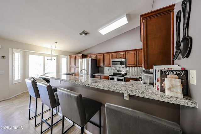4558 E Libby St, Phoenix, AZ 85032 - kitchen featuring appliances with stainless steel finishes, a peninsula, lofted ceiling, light stone counters, and a kitchen bar