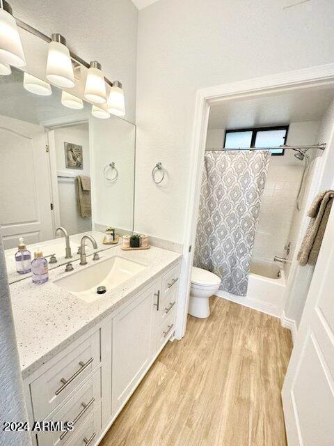 full bathroom featuring hardwood / wood-style flooring, vanity, shower / tub combo, and toilet