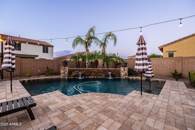 pool at dusk featuring a fenced in pool, a fenced backyard, and a patio area