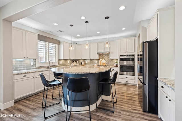 kitchen featuring under cabinet range hood, appliances with stainless steel finishes, a center island, and dark wood-type flooring