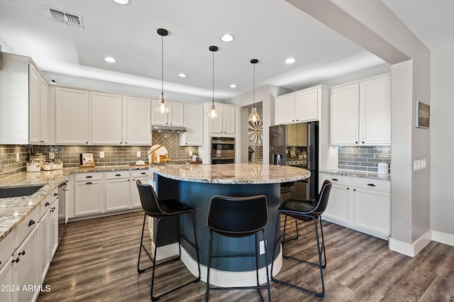 kitchen featuring dark wood-style floors, visible vents, stainless steel appliances, under cabinet range hood, and a center island